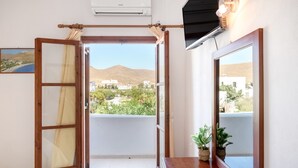 Ein Zimmer mit einem Bett, einer Holztür, einem Fenster und Blick auf Gebäude und Berge.