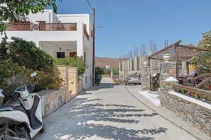A narrow street with a white building, a parked scooter, and a car.