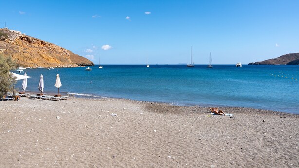 Ein Strand mit sandigem Ufer, einigen Sonnenschirmen und Booten im Wasser.