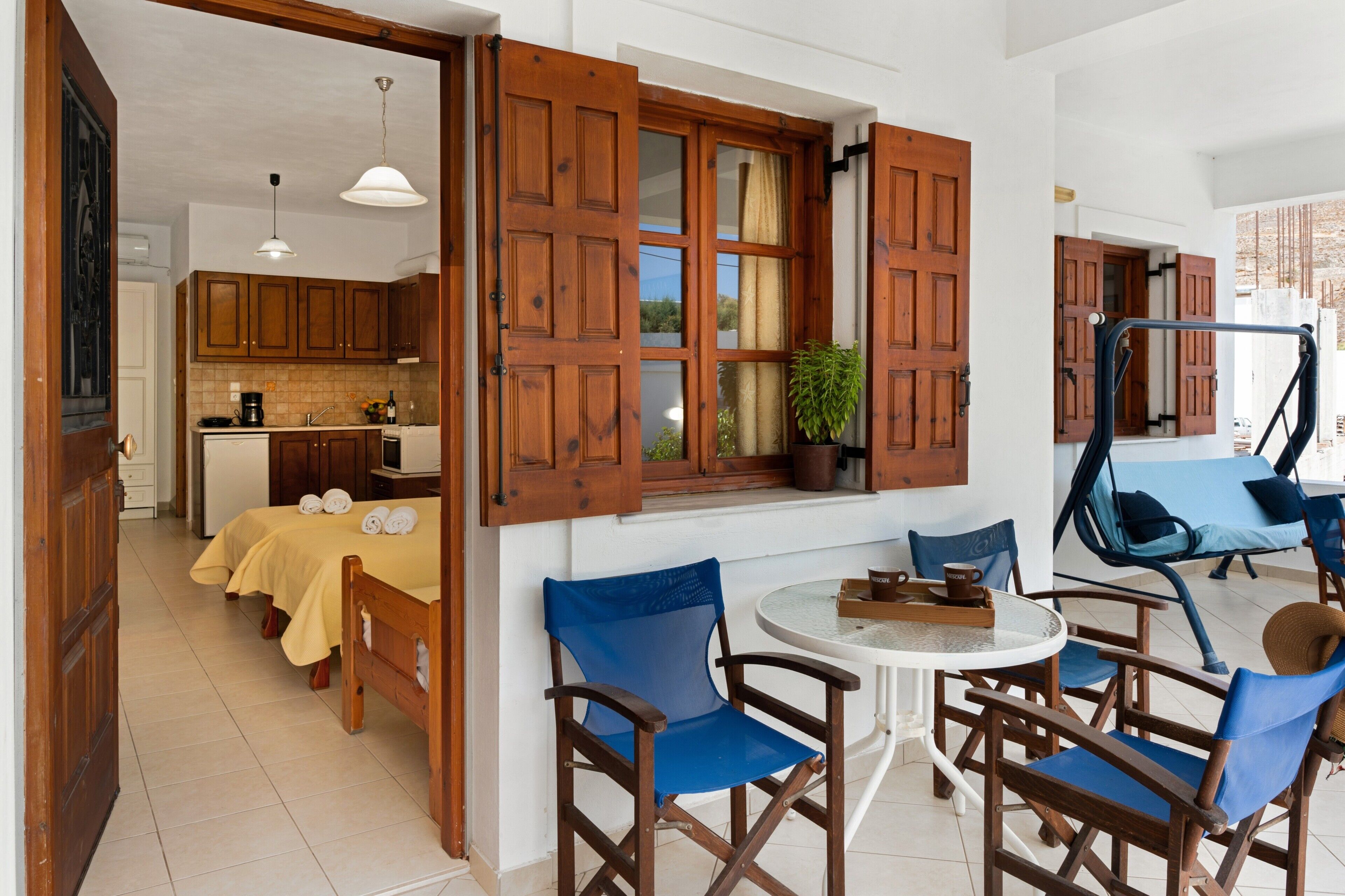 A room with a bed, wooden chairs, a round table, and a window with open shutters.