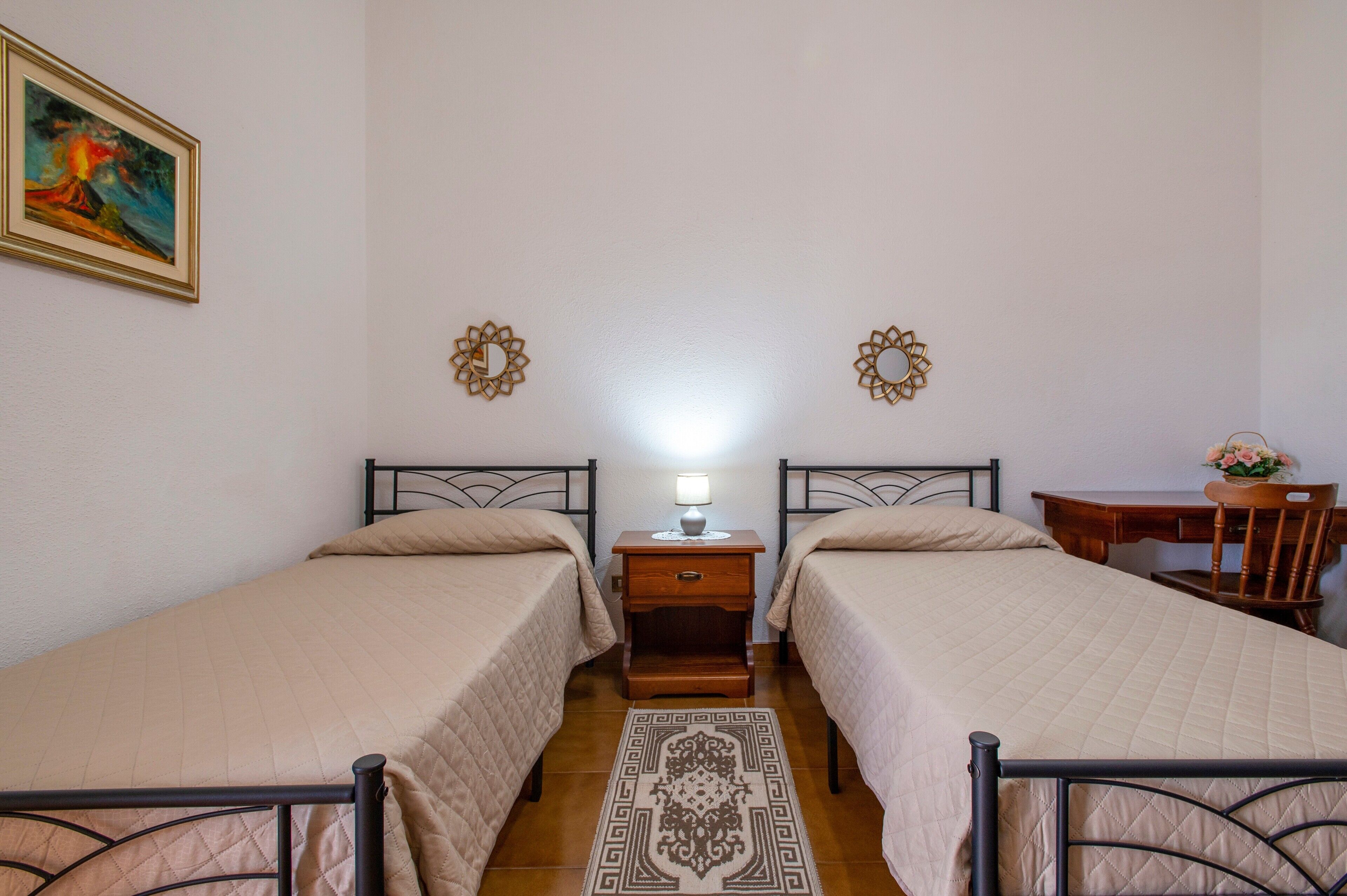 Ein Zimmer mit zwei Betten, einem Nachttisch mit Lampe, einem Schreibtisch und einem Stuhl.