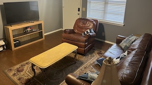 A living room with a television on a wooden stand, a brown leather chair, a brown leather sofa, and a patterned rug. - Great location close to all Tulsa has to offer.  Pet friendly, fenced back yard! (Tulsa)