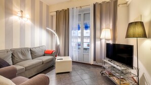 A living room with a sofa, a small coffee table, a TV on a stand, and a lamp. - Apartment 'Florence' with Balcony, Wi-Fi and Air Conditioning (Nice)