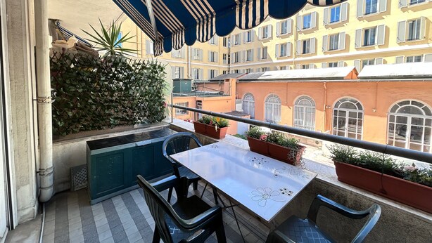 A balcony with a table and chairs, a potted plant, and a view of a building with multiple windows. - Apartment 'Florence' with Balcony, Wi-Fi and Air Conditioning (Nice)