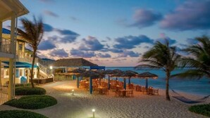 Ein Hotel direkt am Strand mit Außengastronomie, Palmen und Meerblick.
