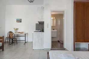 A hotel room with a bed, a dining table with chairs, a small kitchenette, and a bathroom visible through an open door.