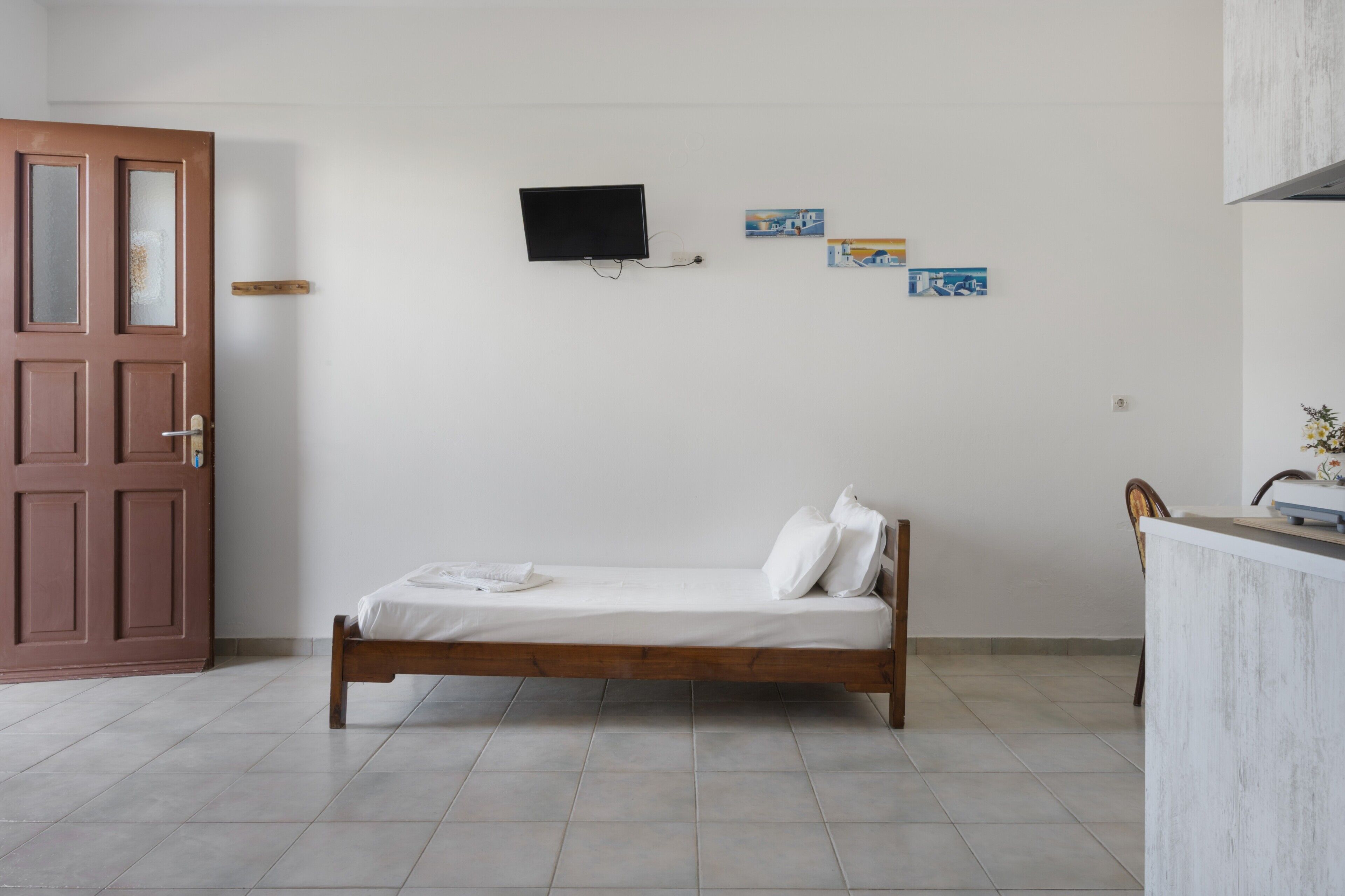 A room with a bed, a TV mounted on the wall, and a small desk with a chair.