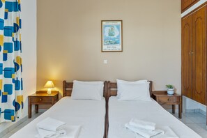 A double bed with white linens, two bedside tables with lamps, a wooden wardrobe, and a framed picture on the wall.