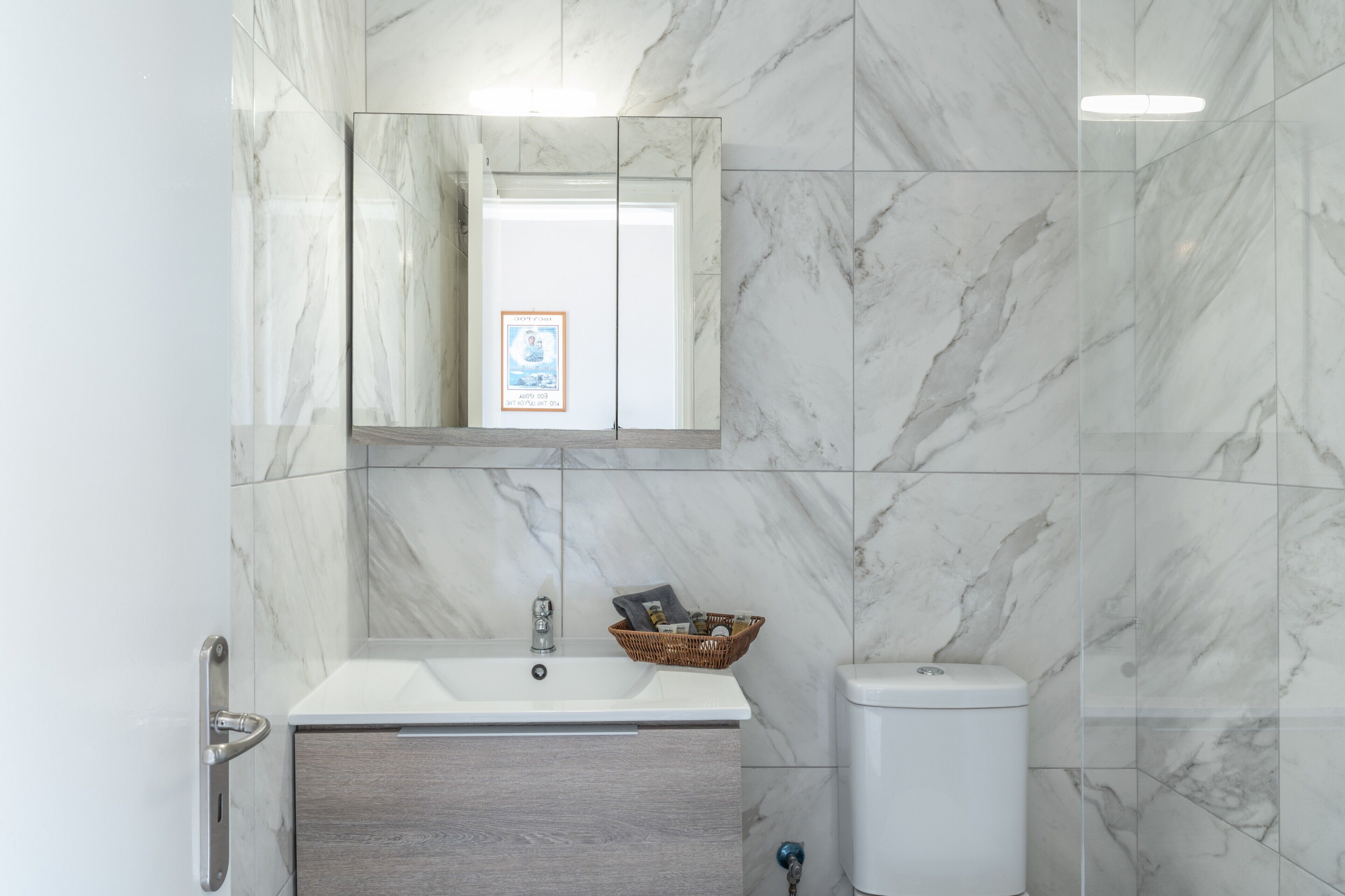 Un baño con pared de mármol, un lavamanos, un espejo y un inodoro.