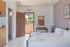 A bedroom with two beds, a wooden door, a desk, and a view of greenery.