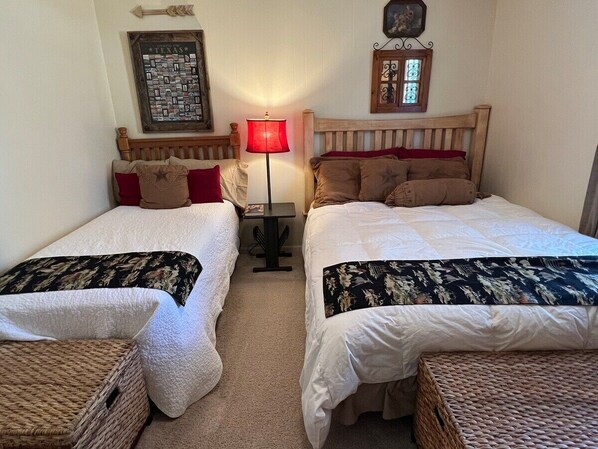 A room with two single beds, a small table, a lamp, and a wall-mounted picture frame.