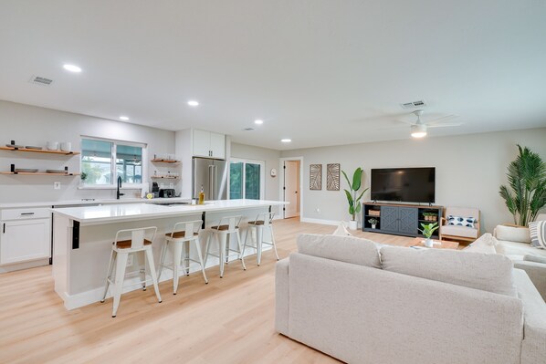 A modern kitchen with a central island, white bar stools, and a dining area. - Cape Coral Home w/ Pool & Boat Dock, 5 Mi to Beach (Cape Coral)