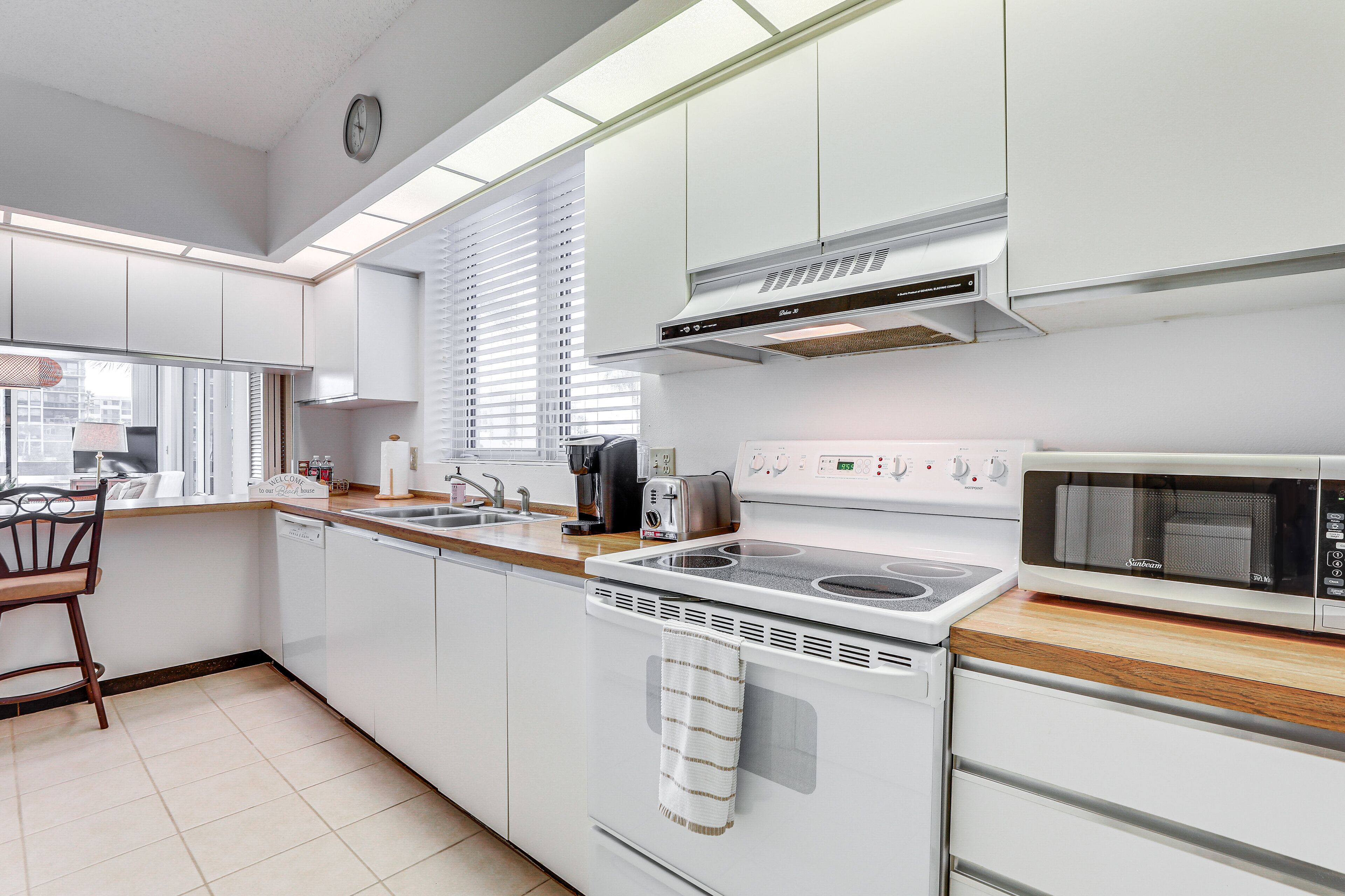A modern kitchen with white cabinetry, a built-in oven, a microwave, and a coffee maker.