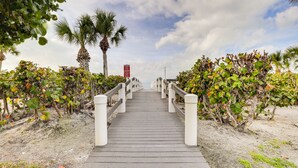 Une promenade en bois mène à une plage bordée de palmiers et agrémentée d’un panneau rouge.