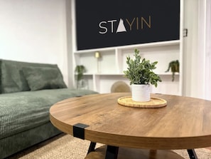 A round wooden table with a potted plant in the center, a green couch, and a wall with the text 'STAYIN'. - The Newington Pool House - With Game Room (Newington)