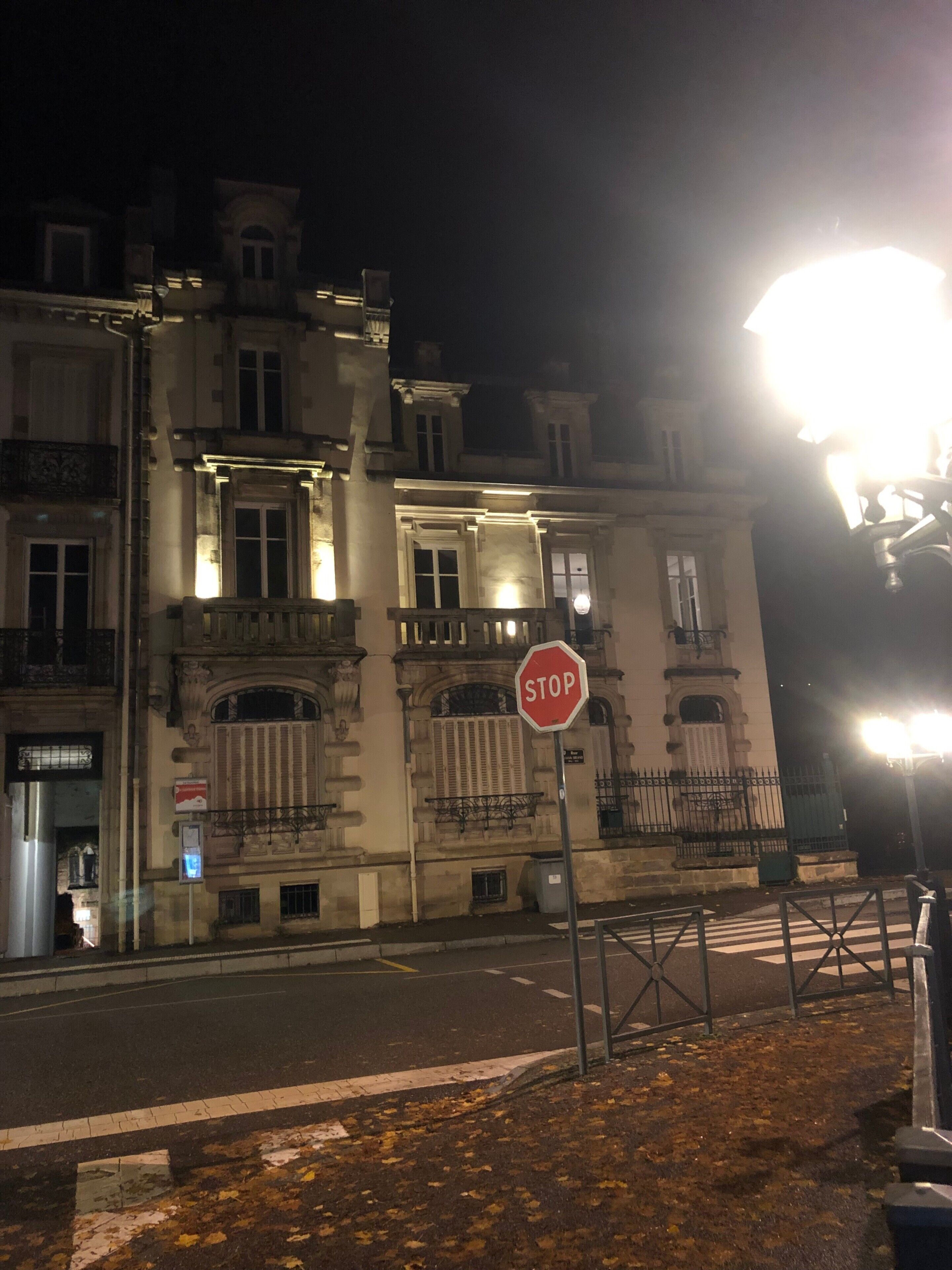 A nighttime street scene with a stop sign in the foreground, a building with classical architecture in the background, and a street lamp illuminating the area.