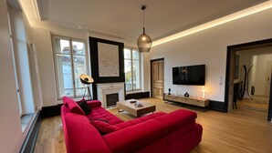A modern living room with a red sofa, a fireplace, a television, and a large window. - Apartment 'L'aristide' with Private Terrace, Balcony and Wi-Fi (EPINAL)
