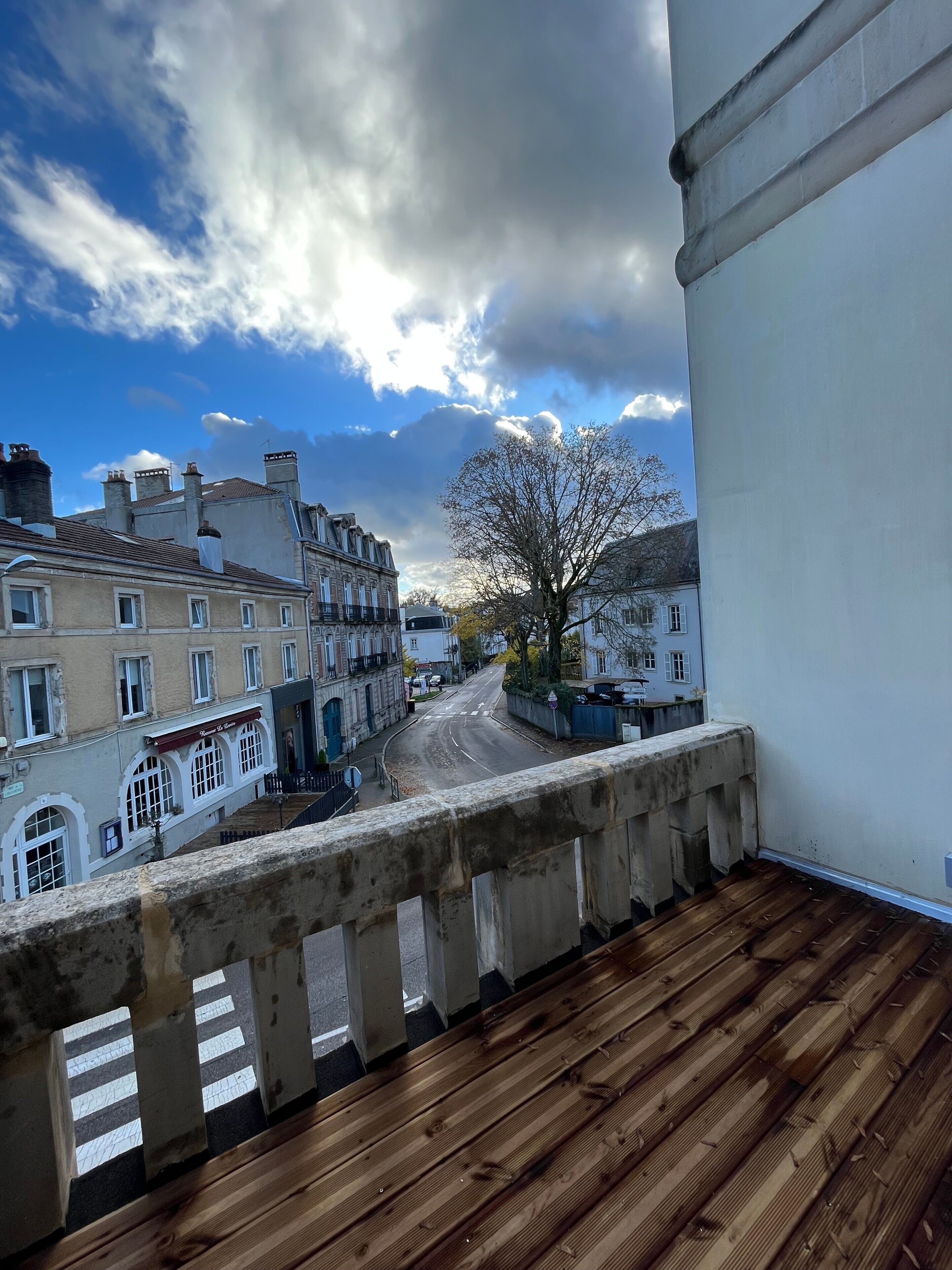 A balcony with a view of a street, buildings, and a tree.