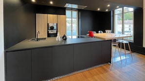 A modern kitchen with a central island, built-in oven, and a dining area with a table and chairs. - Apartment 'L'aristide' with Private Terrace, Balcony and Wi-Fi (EPINAL)