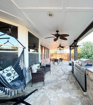 Eine überdachte Terrasse mit einer Hängematte, Sitzgelegenheiten im Freien, Deckenventilatoren und einem Grill.