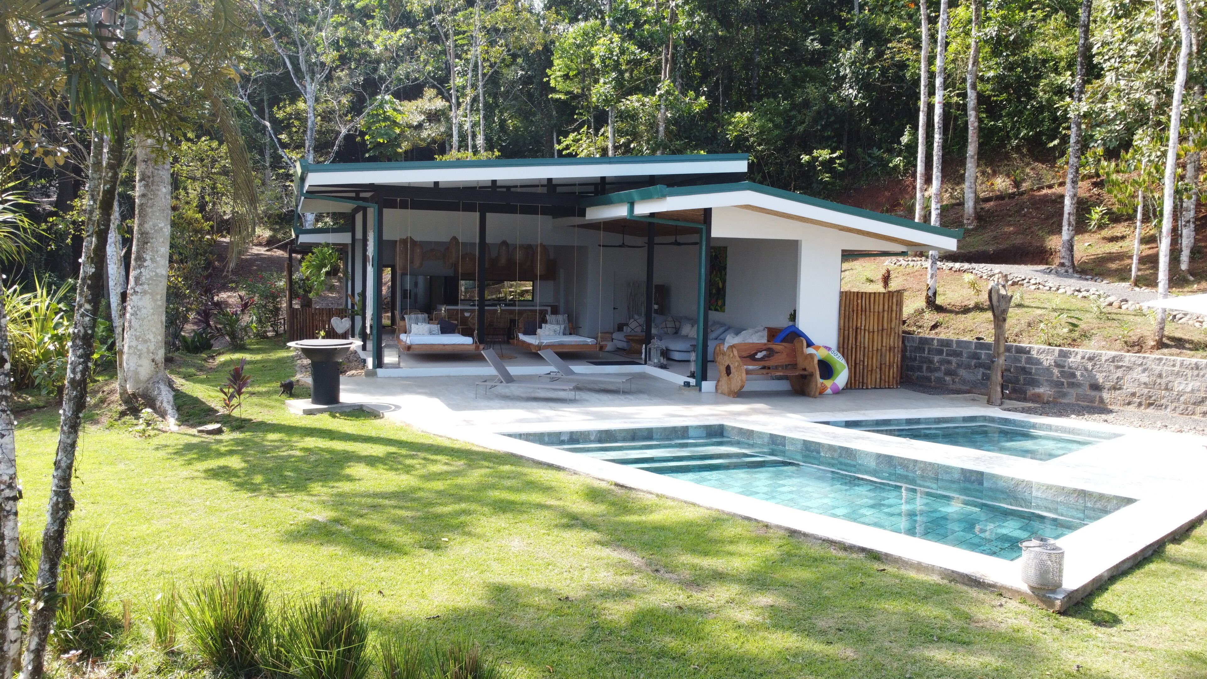Un área de estar exterior moderna con piscina, sillas de descanso y un espacio cubierto para sentarse.