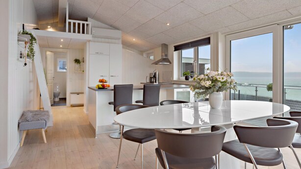 A modern kitchen with white cabinets, a dining area with a round table and chairs, and a view of the sea through large windows. - Awesome home in Haderslev (Haderslev)
