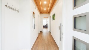 Un pasillo con suelo de madera, paredes blancas y techo de madera. Se observan cuadros enmarcados en las paredes y un perchero a la izquierda.