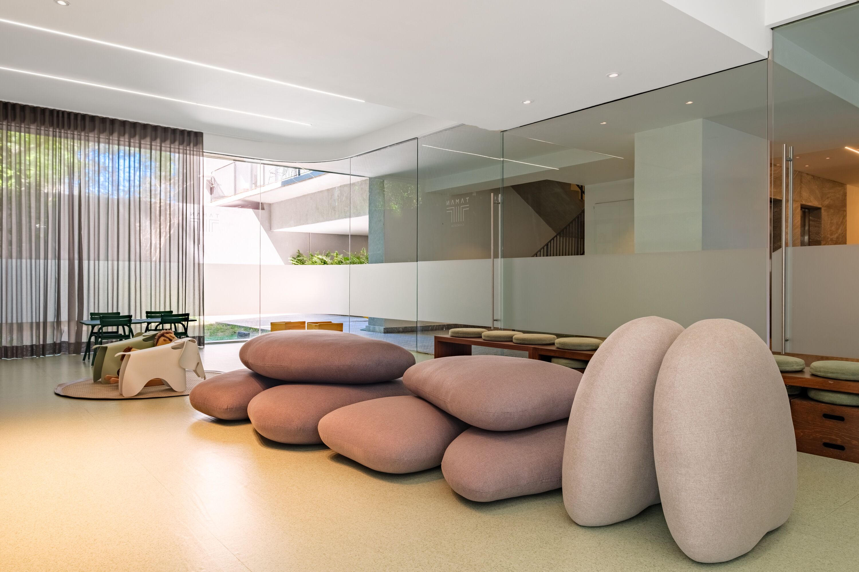 Ein modernes Interieur mit einer Sitzecke, ausgestattet mit großen, abgerundeten Kissen, einer Glastrennwand und einer Treppe, die in einen oberen Bereich führt.