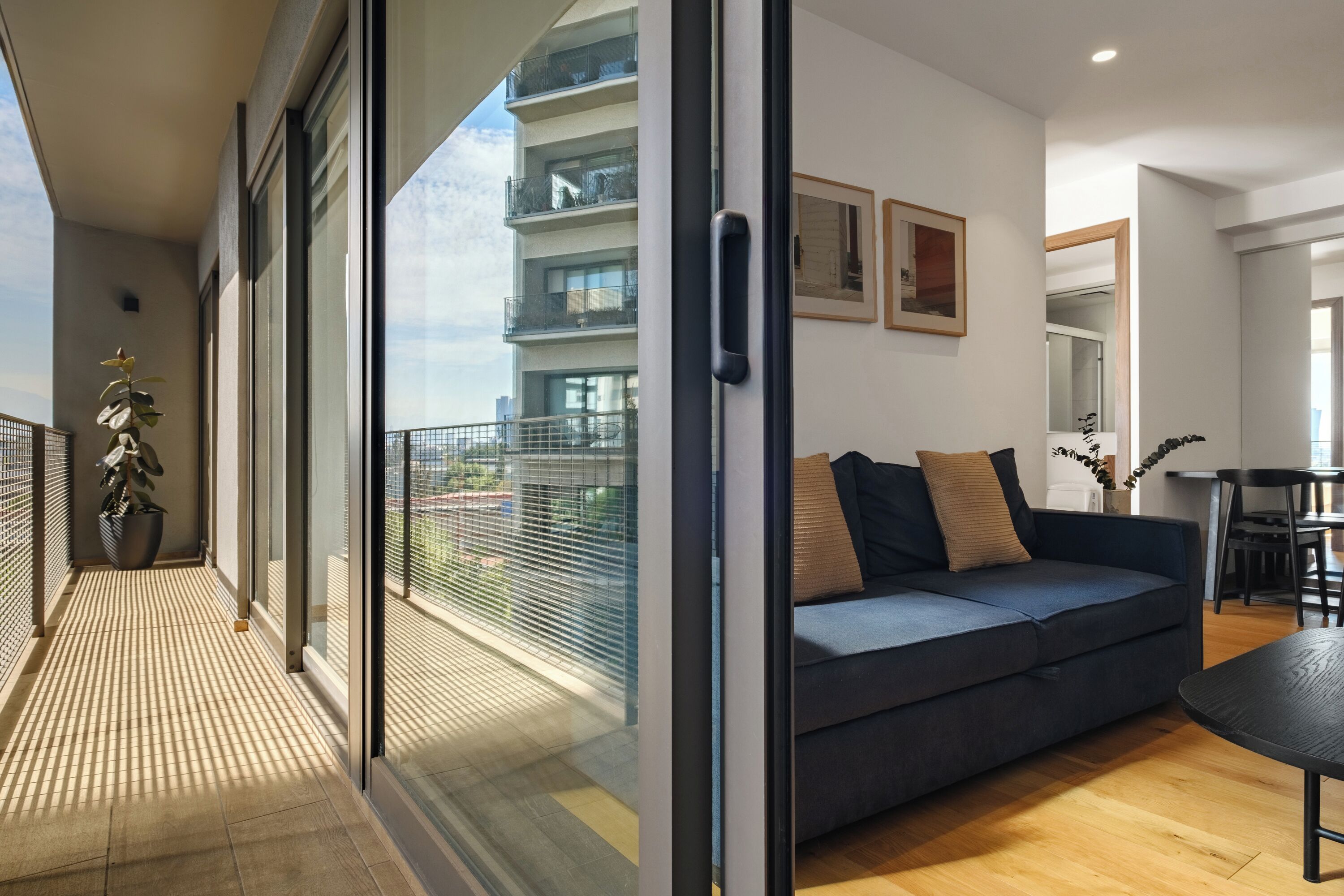 A modern living room with a sofa, a dining table, and a balcony with a view of other buildings.
