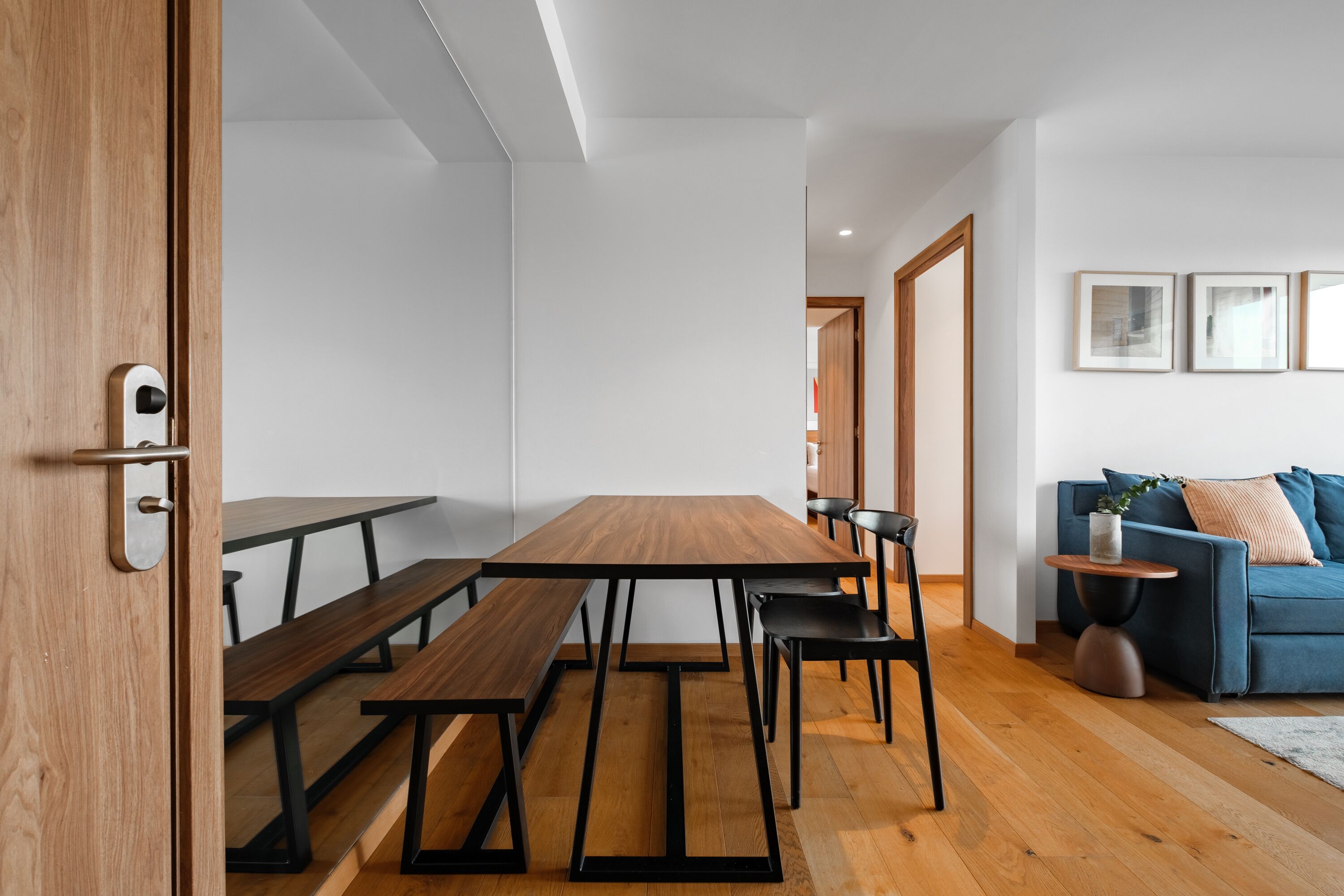 A modern dining area with a wooden table and benches, a blue sofa, and a small side table with a plant.