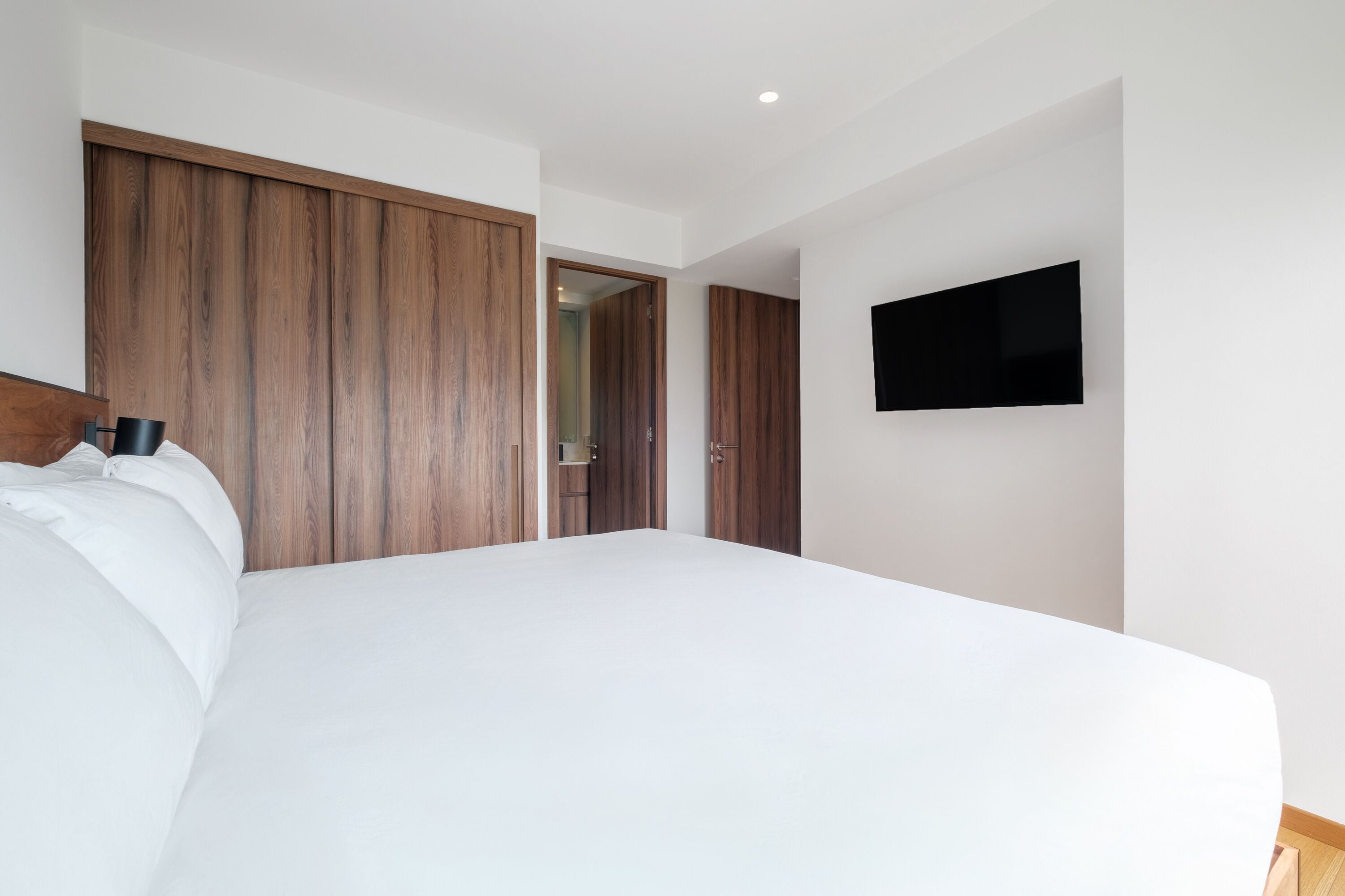 A bedroom with a large bed, wooden wardrobe, and a flat-screen TV mounted on the wall.