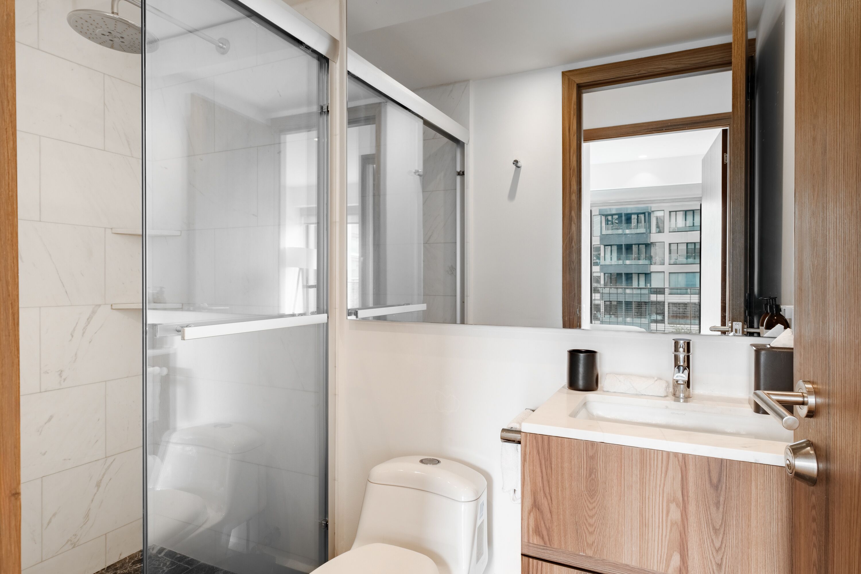 A modern bathroom with a glass shower enclosure, a toilet, and a sink with a wooden vanity.