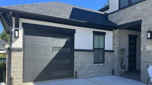 A modern house with a garage, stone facade, and a small garden area. - Serenity Pines, one bedroom, one bathroom apartment with full kitchen and garage (Pinehurst)
