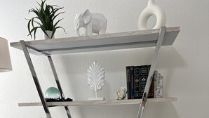A multi-tiered metal shelving unit with decorative items and books. - Serenity Pines, one bedroom, one bathroom apartment with full kitchen and garage (Pinehurst)