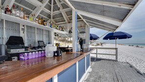 Een strandbar met een houten toonbank, flessenrekken en parasols.