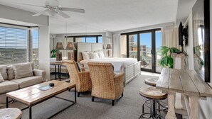 A modern hotel room with a large bed, a sofa, two armchairs, a coffee table, and a dining table.