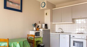 Compact kitchen with dining area, featuring a table, chair, refrigerator, microwave, coffee maker, and sink with modern faucet.