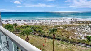 Blick auf den Strand vom Balkon aus, mit Palmen und einem Zaun.