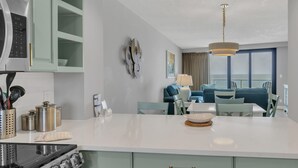 A modern kitchen with a central island, a dining area with a view, and a living room with a sofa and lamp. - Gulf Views & Golf Cart: Luxe Seaside Retreat (Miramar Beach)