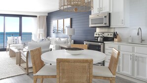 Una cocina moderna con armarios blancos, un microondas y una estufa. Hay una zona de comedor con una mesa redonda y sillas de mimbre.