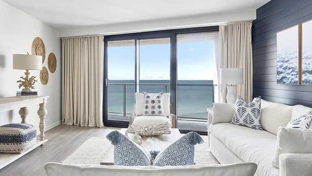 Una sala de estar moderna con un gran ventanal con vista al mar, un sofá blanco, una mesa de centro y decoración en las paredes.