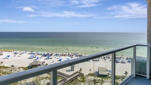A beach view from a balcony with a railing, sandy beach, umbrellas, and a lifeguard tower. - "Beachside Serenity: 9th-Floor 1-Bedroom Condo with Gulf Views, Sleeps 4!" at Sandestin Golf and Beach Resort! (Miramar Beach)