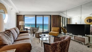 A modern hotel room with a large window offering a view of the ocean, a sofa, a leopard print armchair, a coffee table, and a flat-screen TV. - "Serene Sunrises: Cozy 10th-Floor Haven with Gulf Views in Beachside Two!" at Sandestin Golf and Beach Resort! (Miramar Beach)