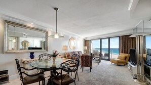 A hotel room with a dining area, a sofa set, a television, and a large window offering a view of the ocean. - "Serene Sunrises: Cozy 10th-Floor Haven with Gulf Views in Beachside Two!" at Sandestin Golf and Beach Resort! (Miramar Beach)