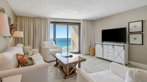 Habitación de hotel con balcón, muebles blancos, televisor de pantalla plana y una mesa de centro de madera.