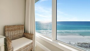 Una silla de mimbre con cojín junto a una ventana con vistas a la playa.