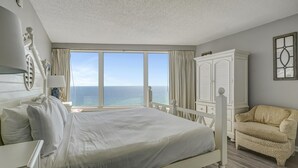 A hotel room with a large bed, a white wardrobe, a leopard print armchair, and a view of the ocean.