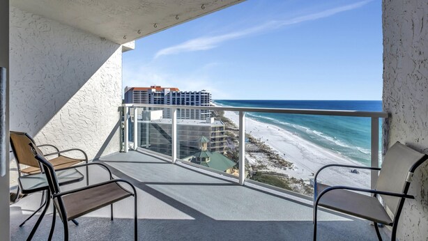 A balcony with a view of the beach and ocean, featuring two chairs and a table.