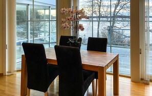 Un coin repas avec une table en bois et quatre chaises, de grandes fenêtres donnant sur un paysage enneigé, et une plante en pot ornée d’orchidées.