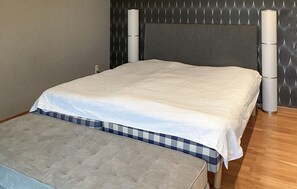 Un lit bien fait, avec une couette blanche et une housse de couette à carreaux, placé contre un mur à motifs, avec deux objets cylindriques de chaque côté.
